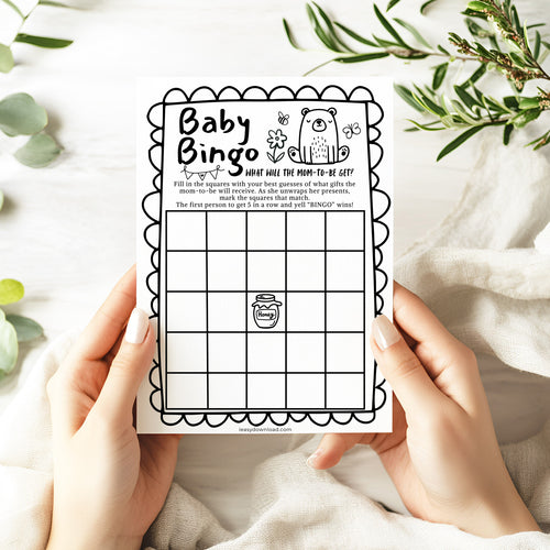 Baby Bingo game card held by hands with a white background and greenery.