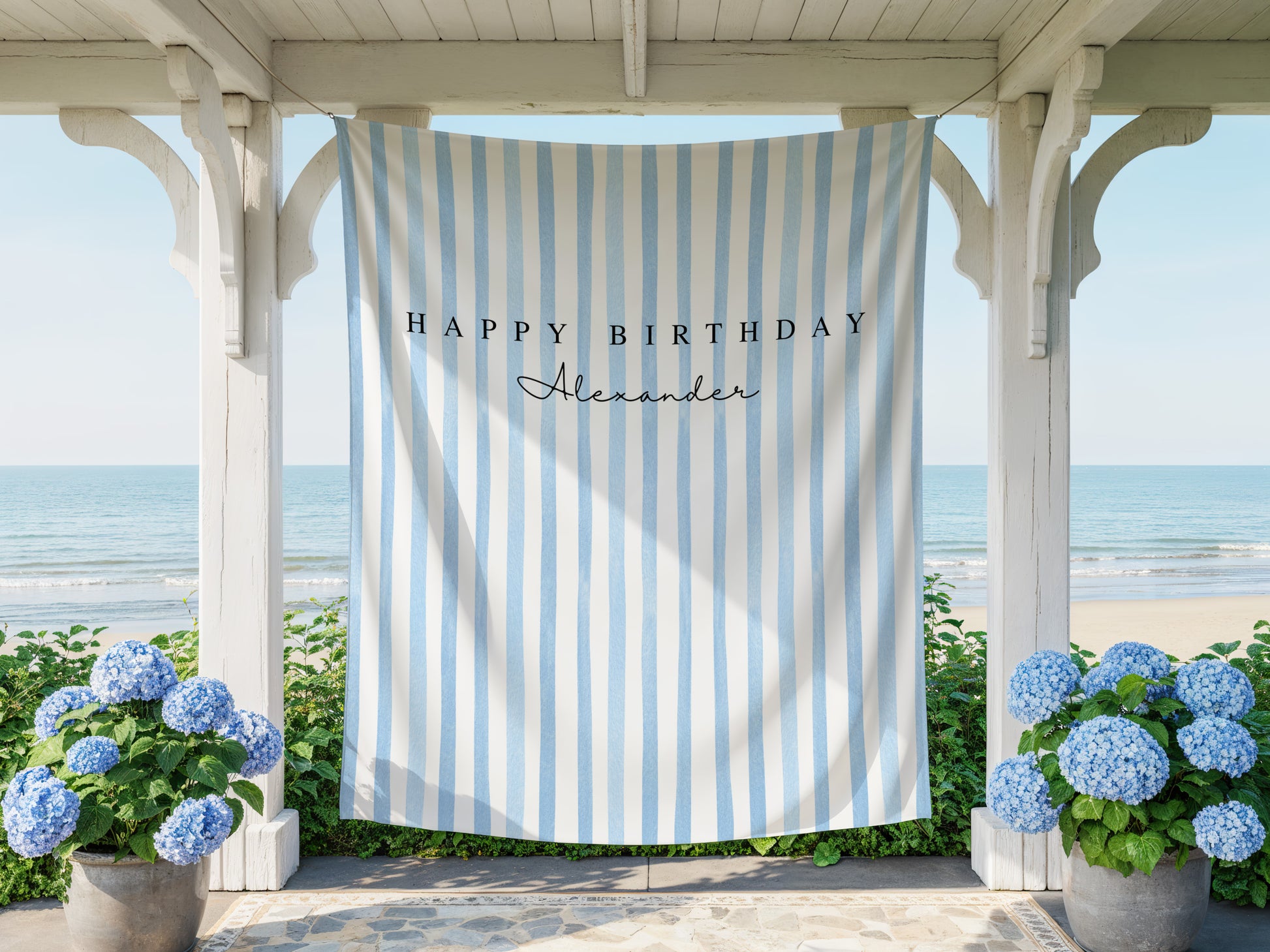 Striped birthday banner with 'Happy Birthday Alexander' text hanging on a gazebo with ocean view.