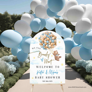 Baby shower welcome sign with balloons and teddy bear design, surrounded by blue and white balloons outdoors.