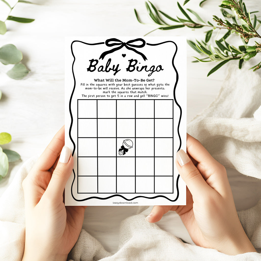 Baby bingo game card held by hands with a white background and greenery