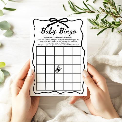 Baby bingo game card held by hands with a white background and greenery